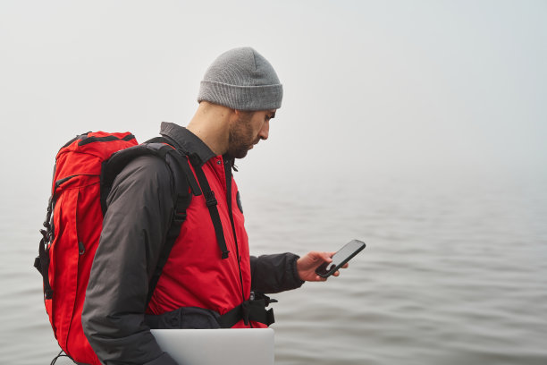 工作自由的理念。男性旅行背包和笔记本电脑在海边检查手机图片下载