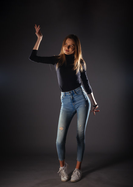 迷人的女模特在牛仔布牛仔裤摆孤立的灰色背景。图片下载