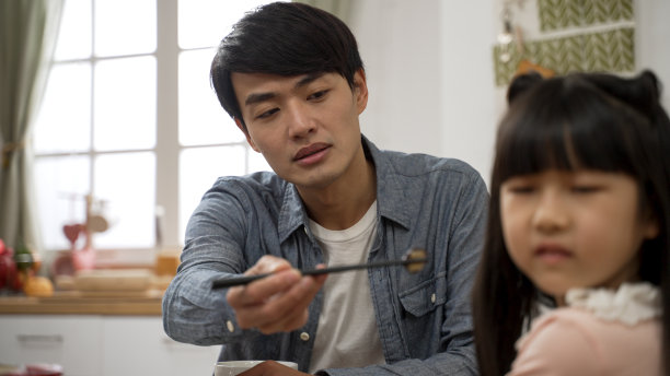 选择性的焦点沮丧的亚洲父亲要求他的女儿吃一口食物在餐厅在家里。他难过地放下筷子，女孩转过头说不图片下载