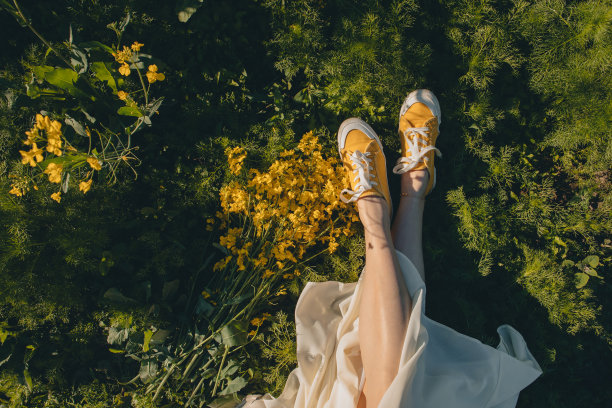 穿着黄色鞋子的女人坐在油菜籽花束旁的草地上图片下载