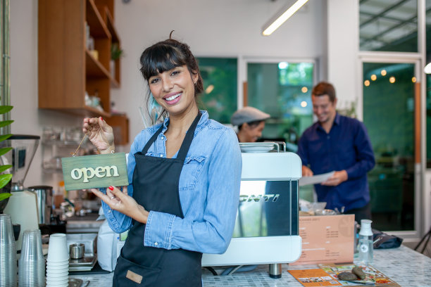 微笑的主人站在她的咖啡馆与开放的招牌的肖像。图片下载