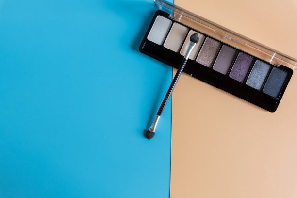 眼影刷在彩色背景上。俯视图的情况下，不同的阴影蓝色，米色和紫色化妆品眼影。各种各样的颜色。美容产品。本空间图片下载