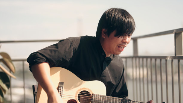 在公寓阳台上弹吉他放松的男人图片下载