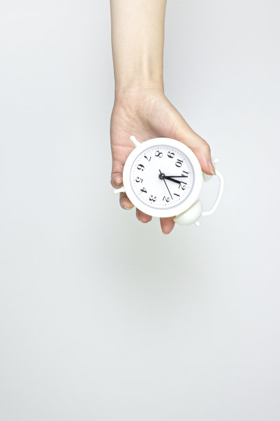 手持灰色背景的老式白色闹钟。业务截止日期，定时器或时间倒计时概念。图片下载