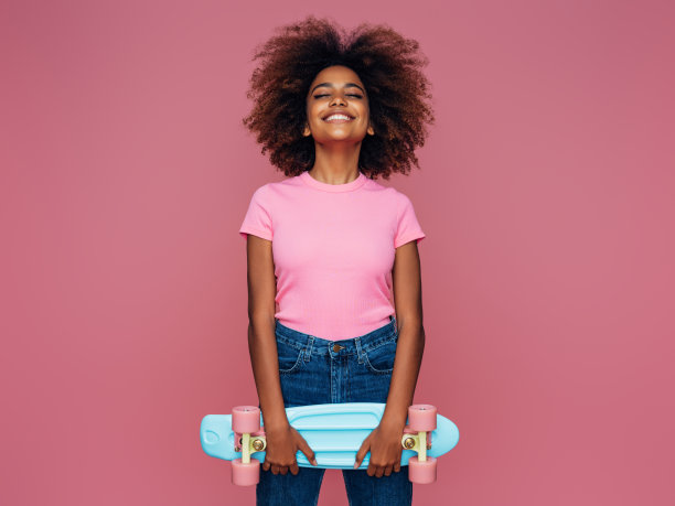 年轻的卷发女孩带着耳机和滑板的照片图片下载