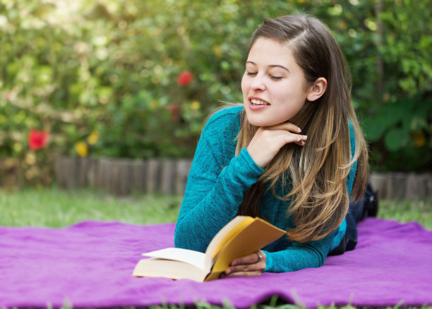 一名美丽的年轻女子躺在一个美丽茂盛的花园里，一边看书，一边沉思图片下载