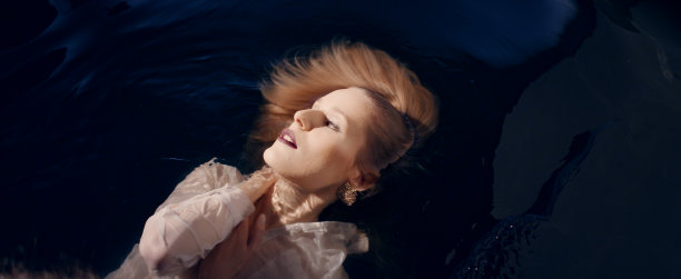 脆弱的女人漂浮在黑暗的水面上。自然美容护理隐喻图片下载