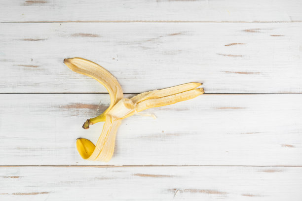 剥了皮的香蕉放在浅色的木质背景上。一个咬香蕉。图片下载