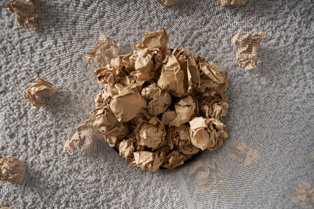 灰色地毯上的垃圾桶底部有棕色的皱巴巴的纸球图片下载