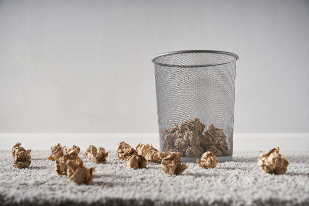 银色地毯上的废纸篓里散落着棕色的皱巴巴的纸球图片下载
