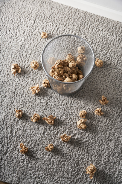 灰色的地毯上放着一个废纸篓，从顶部看，废纸篓周围是皱巴巴的纸球图片下载