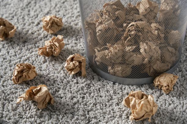 灰色地毯上有一个废纸篓，里面和周围都是皱巴巴的纸球图片下载