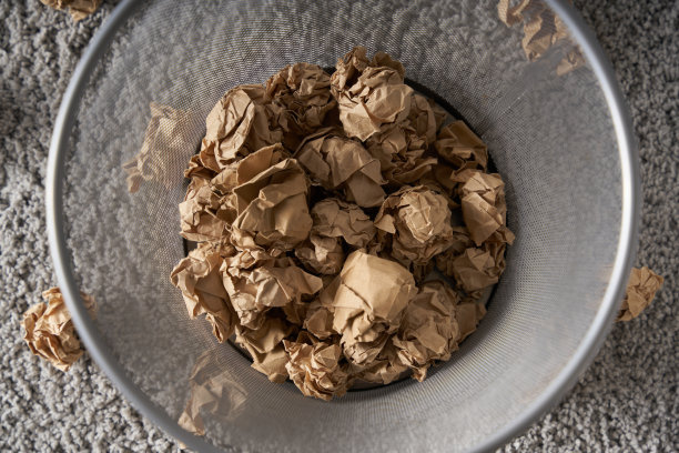 一个废纸篓放在灰色的地毯上，里面装满了棕色的皱巴巴的纸球图片下载