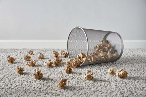 一个掉在地上的废纸篓，里面有皱巴巴的纸球，掉在灰色的地毯上图片下载