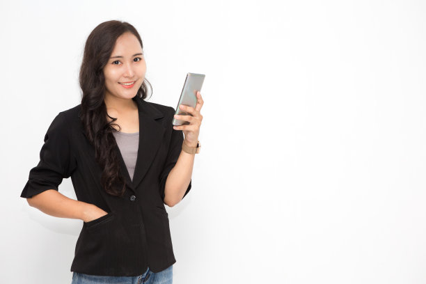 美丽的亚洲商业妇女穿着黑色的西装，在白色的背景和复制空间持有智能手机。自信的亚洲职业女性，微笑开朗图片下载