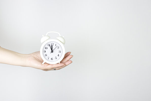 手持灰色背景的老式白色闹钟。手握闹钟的局部视图。图片下载