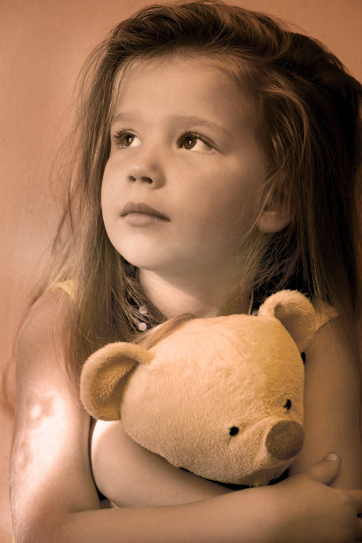 沉思悲伤的小女孩和他的泰迪熊朋友在家里的日落，柔和的光线，阴霾的滤镜图片下载