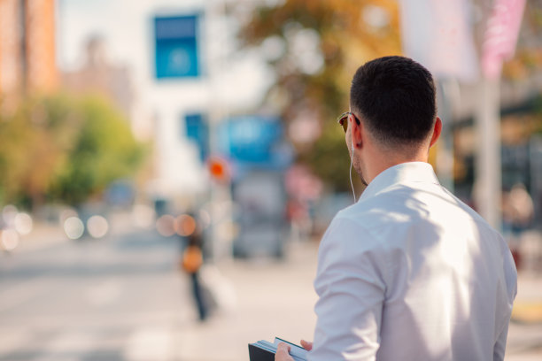 举着手的城市商人在街上，他手里拿着一件外套和一本书，试图赶一辆出租车。图片下载