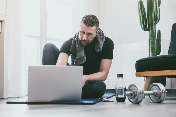 在家锻炼后休息的运动型男人。在笔记本电脑上看健身视频的健美男孩。强壮的男性在客厅上在线体操课。养生运动、训练理念图片下载