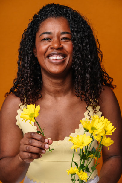 中腰肖像的快乐的非洲妇女，拿着一朵雏菊与白色的微笑。图片下载