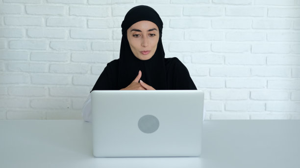 一位穆斯林妇女使用新技术与外界沟通。一名戴着黑色头巾的女性用笔记本电脑通过视频会议与同事交流图片下载