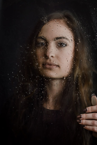 模糊的水滴-美丽的长发年轻女子拿着一个玻璃板覆盖的水滴在她的面前，专注于水滴图片下载