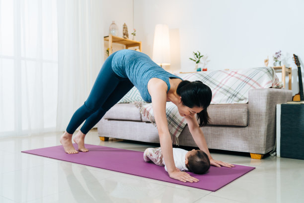 千禧一代的女性在家里做下犬式时，正与宝宝对视。产后锻炼和健康的生活方式图片下载