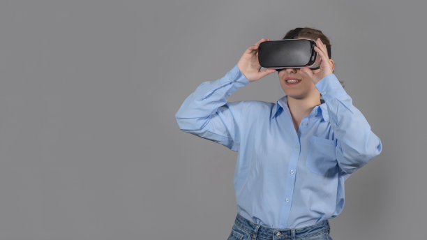 年轻女子戴着虚拟现实眼镜站在科技前沿。工作室在灰色背景前拍摄。元世界VR虚拟现实游戏，元世界概念。图片下载