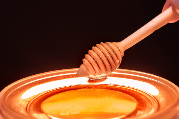 木勺在黑色的背景下从透明的碗里收集蜂蜜图片下载