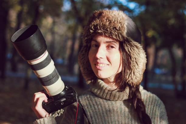 现代相机与一个大镜头在年轻的摄影师女孩手中，准备拍摄照片。小女孩微笑着，拿着相机摆姿势。软的焦点。图片下载