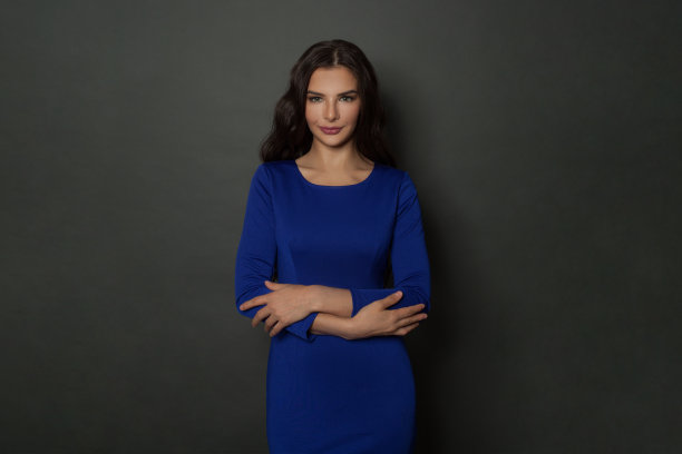 自信的黑发女人在蓝色长裙的肖像。成功的女性模型在深灰色背景与copyspace图片下载