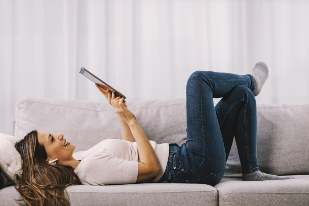 一个女人躺在沙发上，在写字板上滚动。图片下载