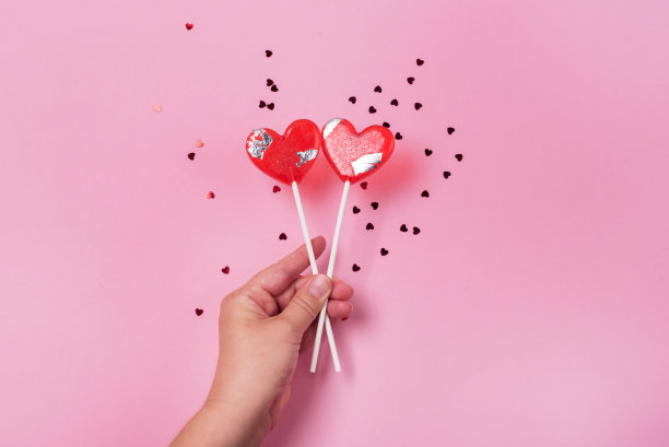 女性手握心形棒棒糖在粉红色的背景心五彩纸屑粉红色的背景水平图片下载