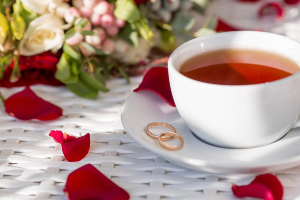 一杯茶，玫瑰花瓣，金婚戒和一束漂亮的花束放在白色的桌子上。婚礼庆典的概念。新娘早上好。图片下载