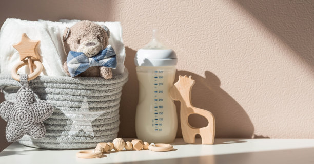 木制玩具，一只熊，鞋子，一瓶牛奶，一堆尿布和婴儿用品在换尿布的桌子上。复制文本的空格。图片下载