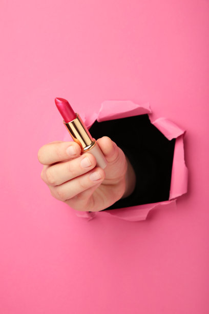 涂着口红的女性手穿过粉红色的纸图片下载
