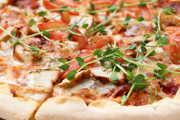 新鲜披萨的特写照片，切片。饰以微绿、番茄、奶酪和肉片。食品的背景。图片下载