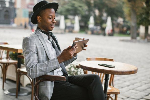 非洲男子在咖啡馆露台上喝着咖啡和平板电脑休息图片下载