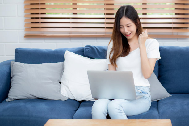 年轻的亚洲商业女性微笑着在家里用笔记本电脑上网，在客厅的沙发上上网，自由职业女孩用笔记本电脑在沙发上舒适，新常态，生活方式的概念。图片下载