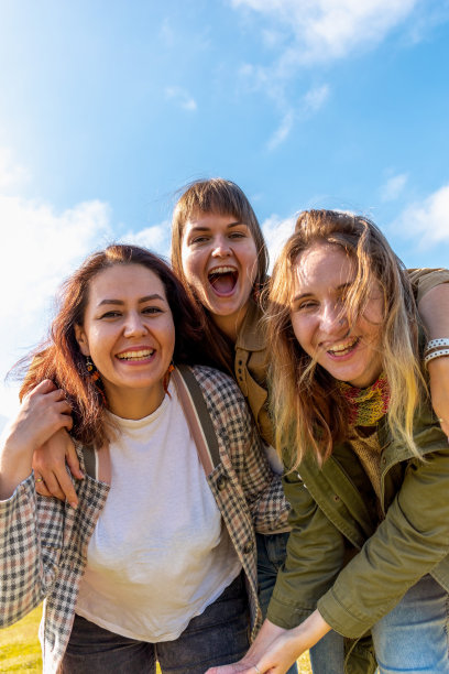 三个不同类型的女朋友正在开心地拥抱。蓝色的天空背景。图片下载