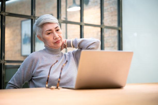 办公室综合症的概念。成熟的亚洲女商人戴着眼镜，使用笔记本电脑，坐在办公桌旁。她伸展手臂，放松脖子图片下载