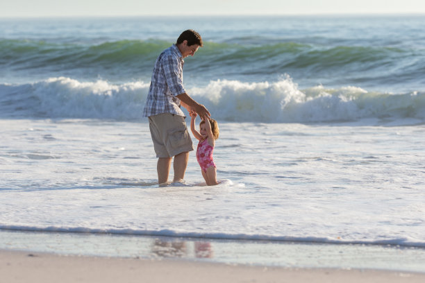 父亲和他的两个小女儿在海滩上玩海浪图片下载