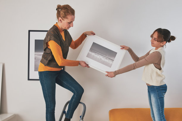 母亲和女儿在家里挂照片和照片。图片下载