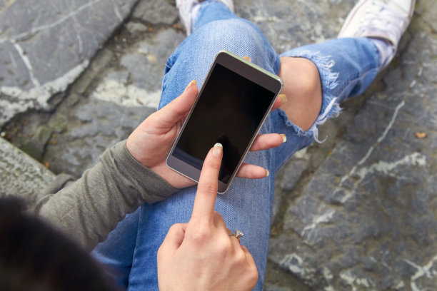 穿着牛仔裤的女人在户外使用现代智能手机。图片下载