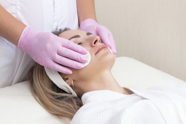 美容。近距离照片可爱的年轻女子与闭着眼睛接受面部清洁程序在美容院。图片下载