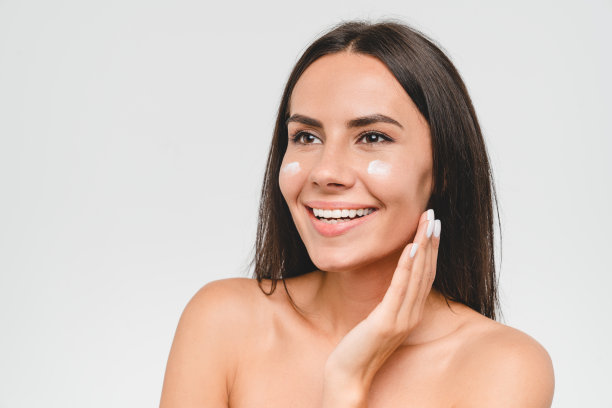 特写肖像的年轻美丽的白人妇女赤膊微笑，应用脸身体霜对她的脸年轻化柔软保湿效果。Spa美容。身体皮肤护理图片下载