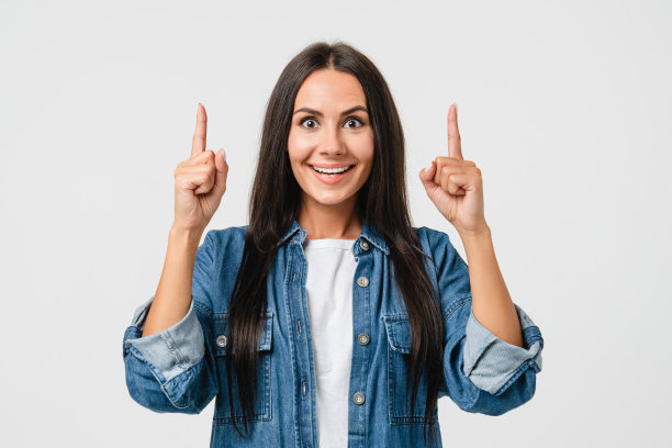 快乐的牙齿微笑年轻的白人妇女在牛仔衬衫看着镜头指着拷贝空间显示自由空间向上孤立在白色背景。图片下载