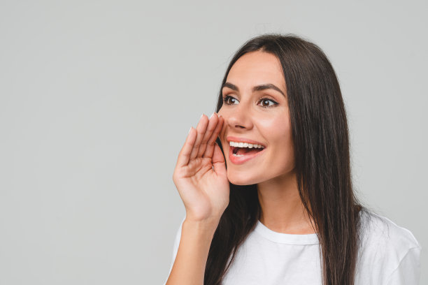 穿着白色t恤的白人年轻女子在灰色的背景下大声喊叫，就像在扬声器里低语打折促销图片下载