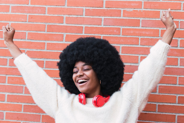 可爱的梦幻有趣的快乐的非洲裔美国妇女脖子上红色耳机，长非洲式头发和完美的白色微笑对着砖墙跳舞，同时有乐趣和微笑图片下载