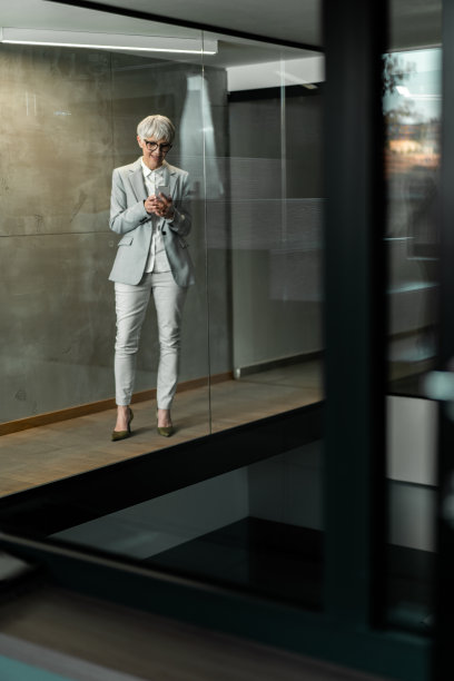 快乐的高级女商人在办公楼走廊使用智能手机。图片下载